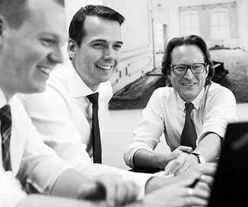 Dr. Oliver Tiegelkamp, LL.M. lachend in Arbeitssituation mit Manuel Thomale und Michael Niemann