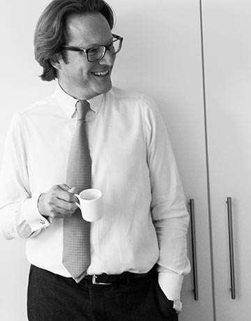 Dr. Oliver Tiegelkamp, LL.M. lachend mit Kaffee